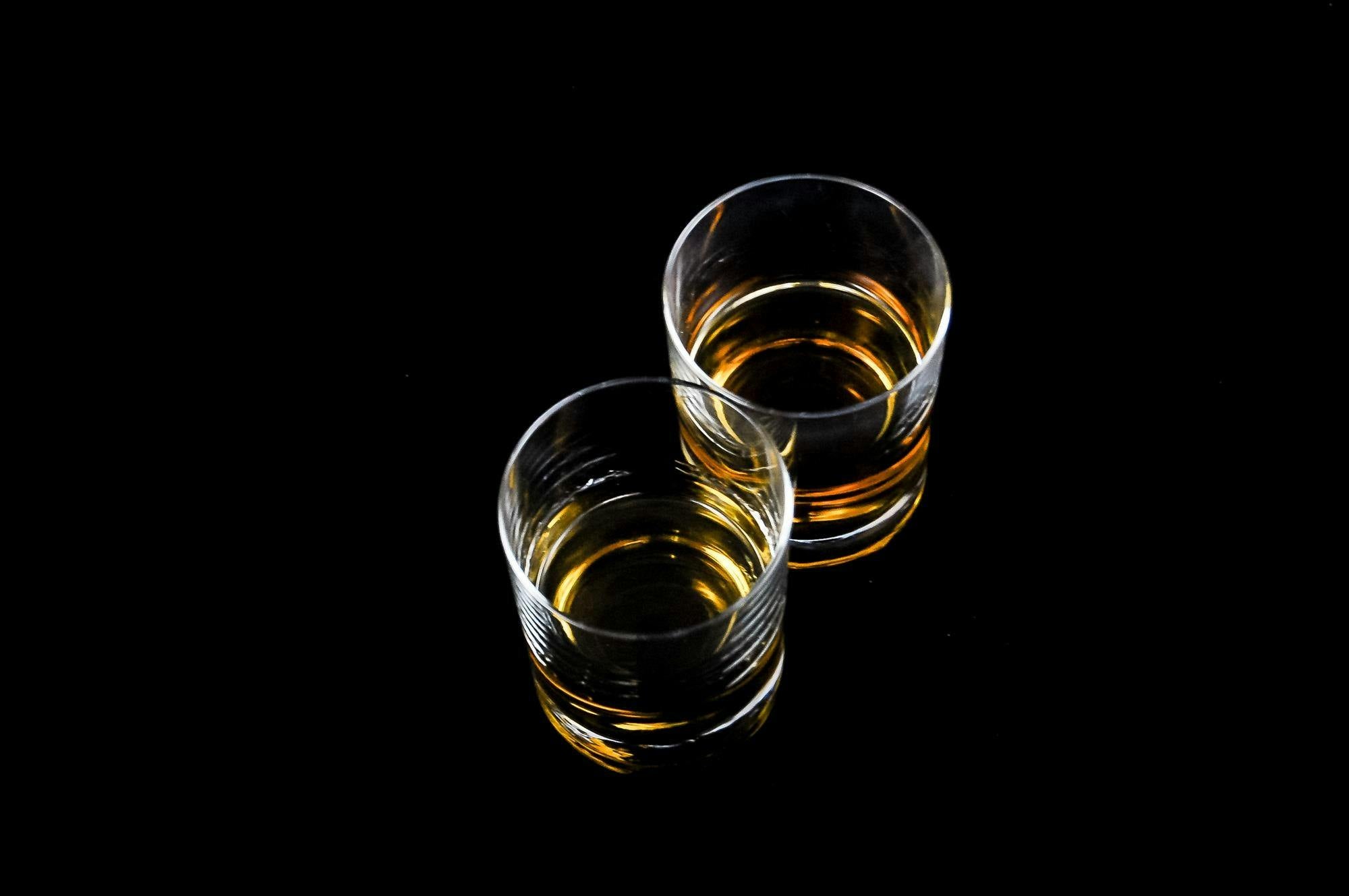 Two glasses of whiskey on a black table.