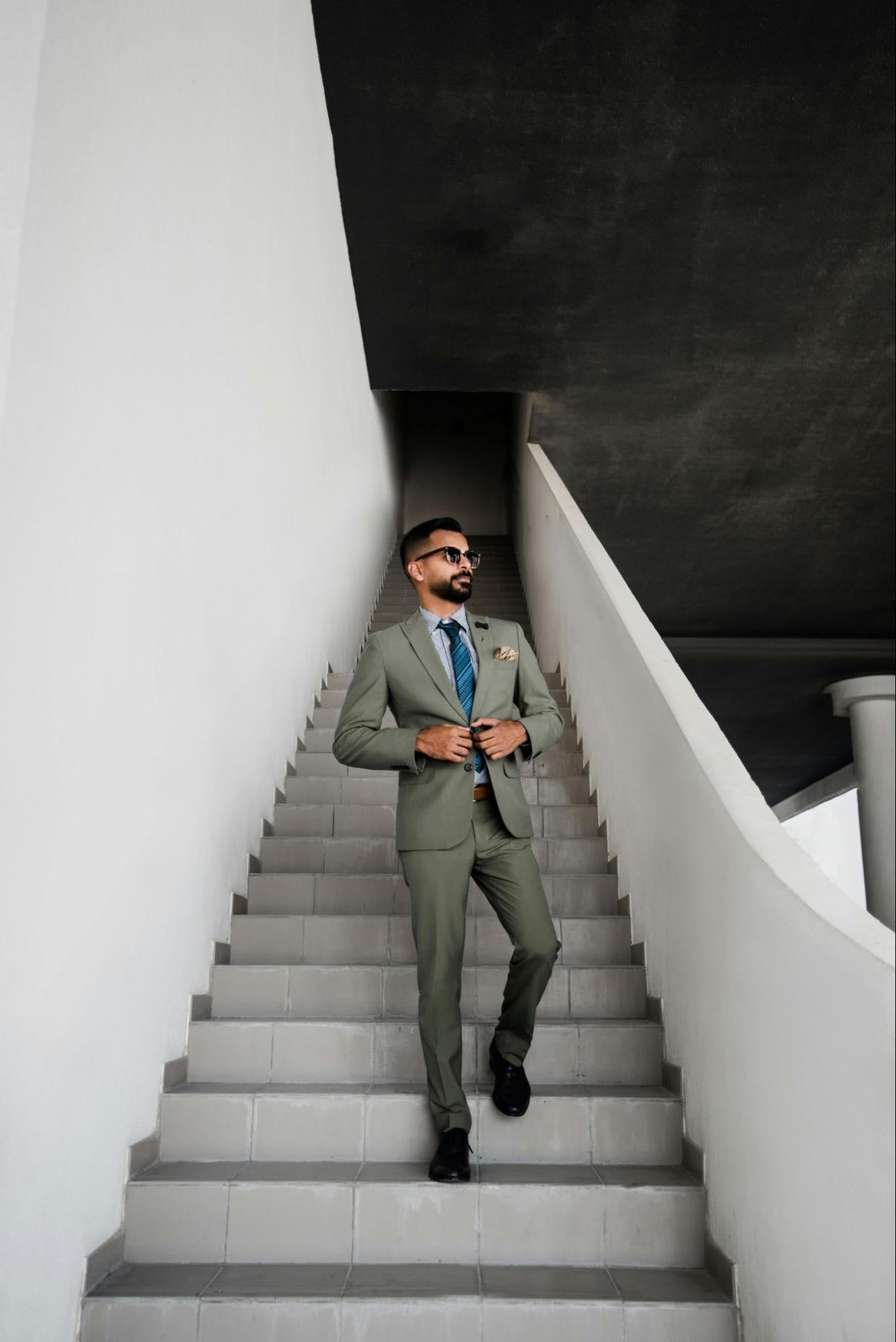 A stylish man in an olive-green suit walks down stone steps.