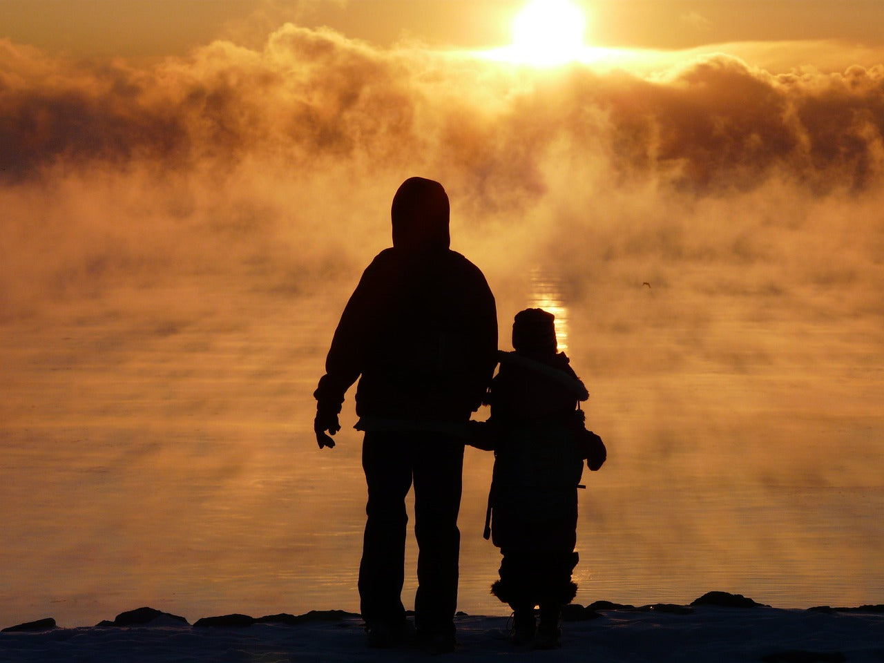 A father and son stand on a hill overlooking a cloudy lake at sunrise