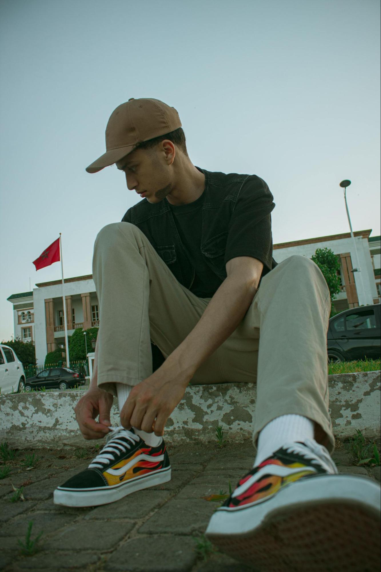 A man wearing khaki pants with a black T-shirt sits on concrete steps outside.