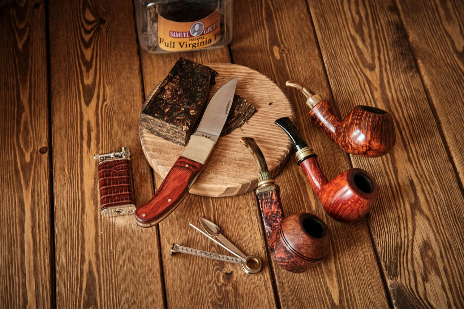 Three pipes, tobacco, a lighter, and a knife are on a table.