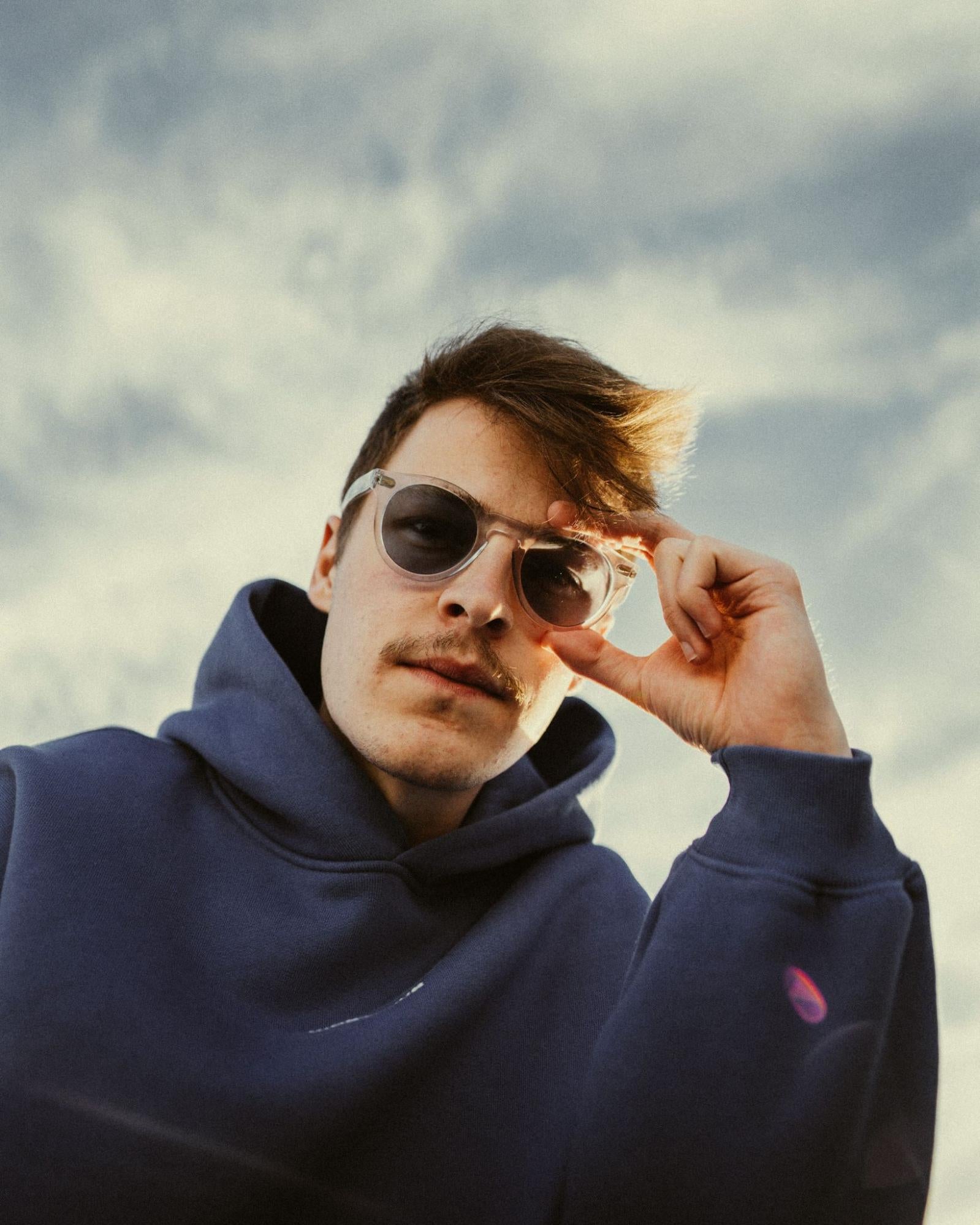 A man wearing a hoodie and sunglasses is standing outside.