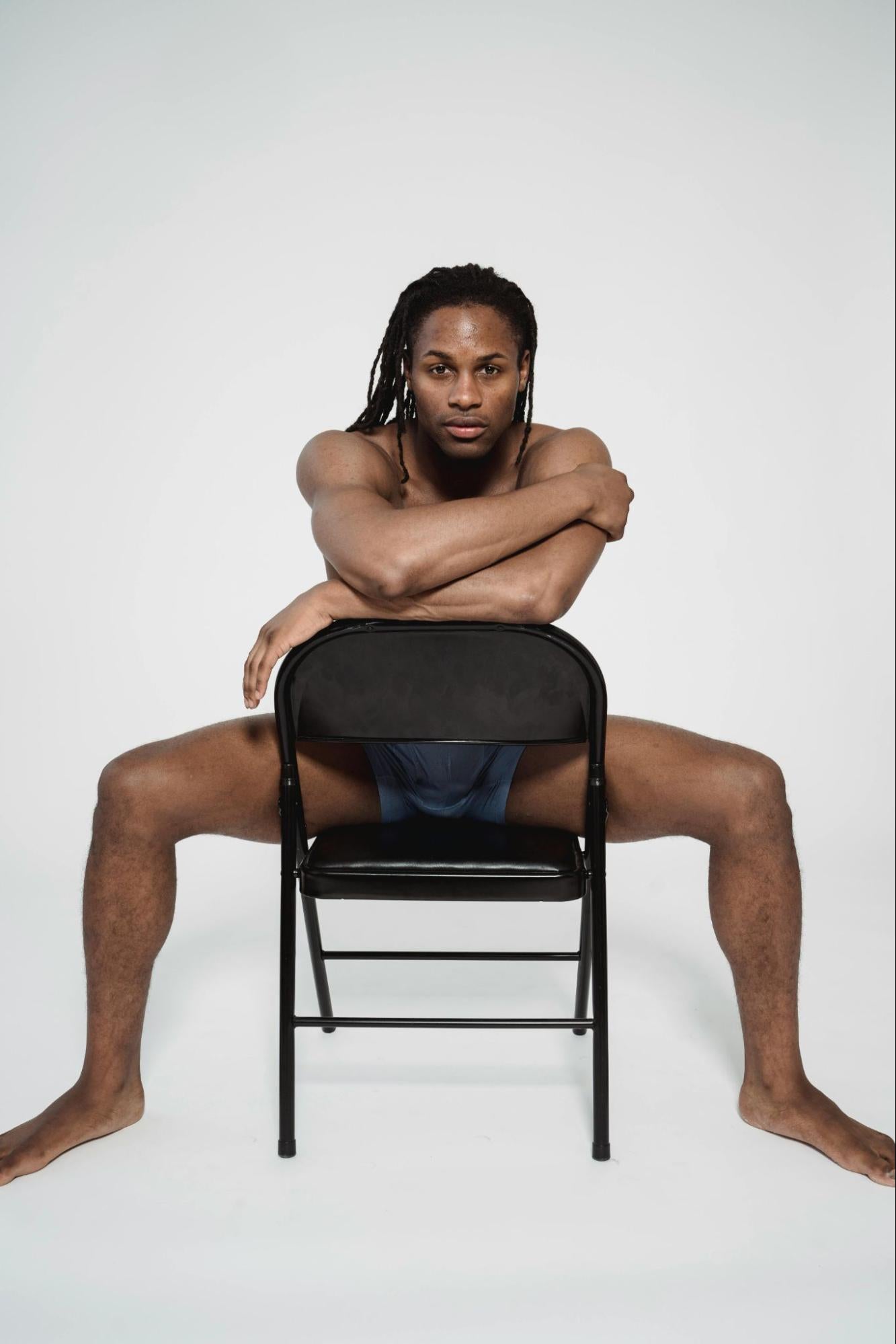 A man wearing boxer briefs sits in a chair.