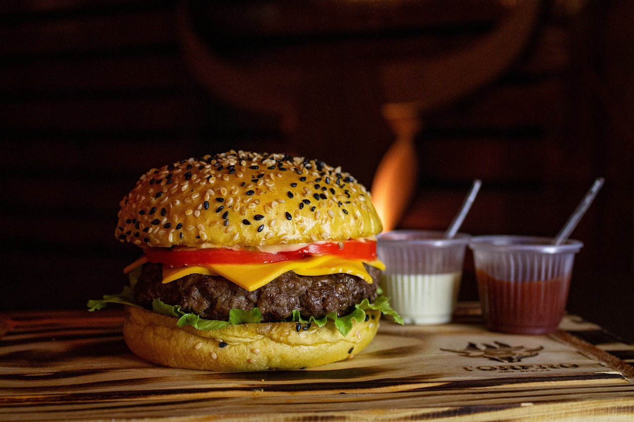 A cheeseburger with condiments on a table near a fireplace.