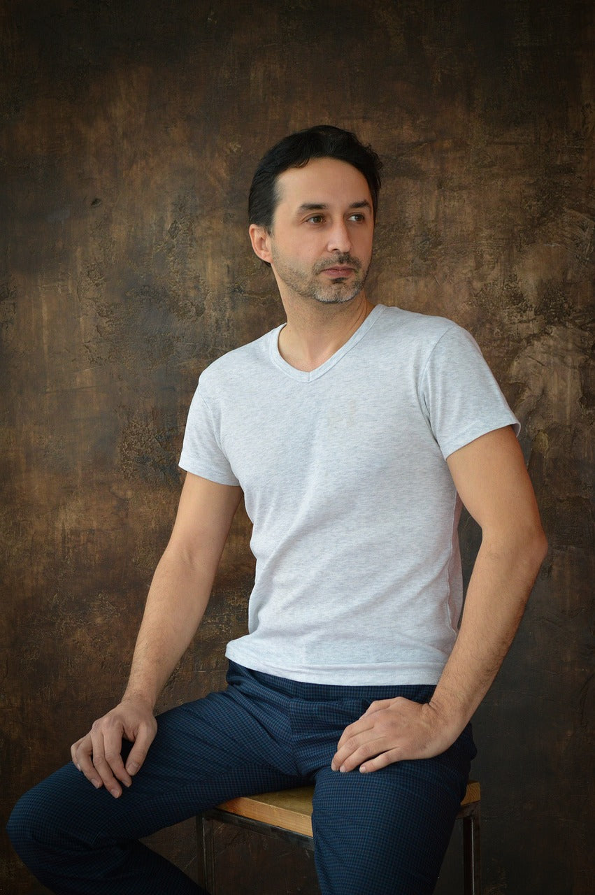 A man wearing a T-shirt and jeans sits on a chair.