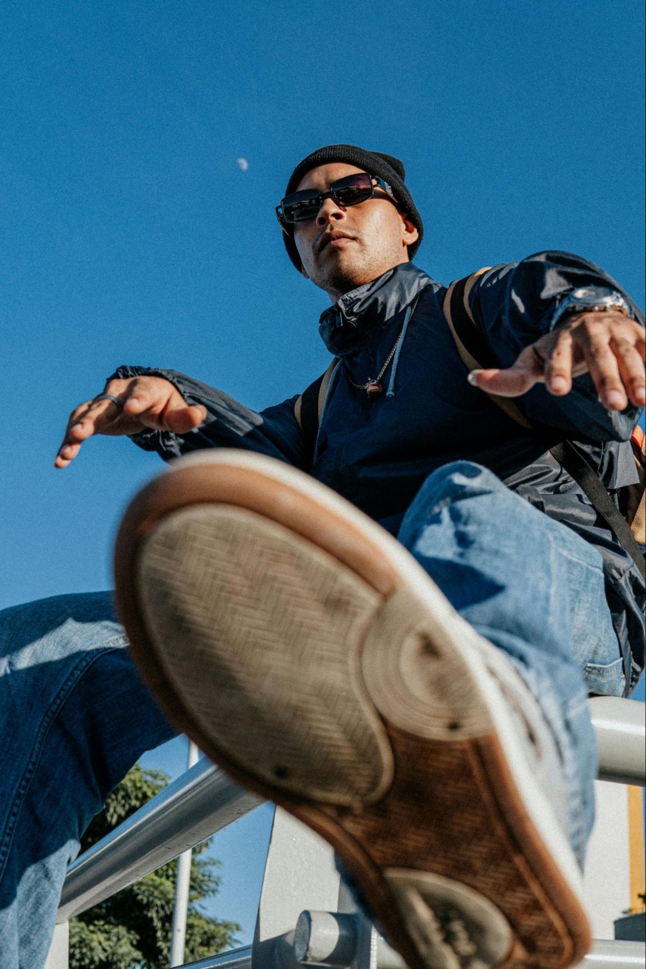 A man in a stylish track jacket sits on a metal railing outside.