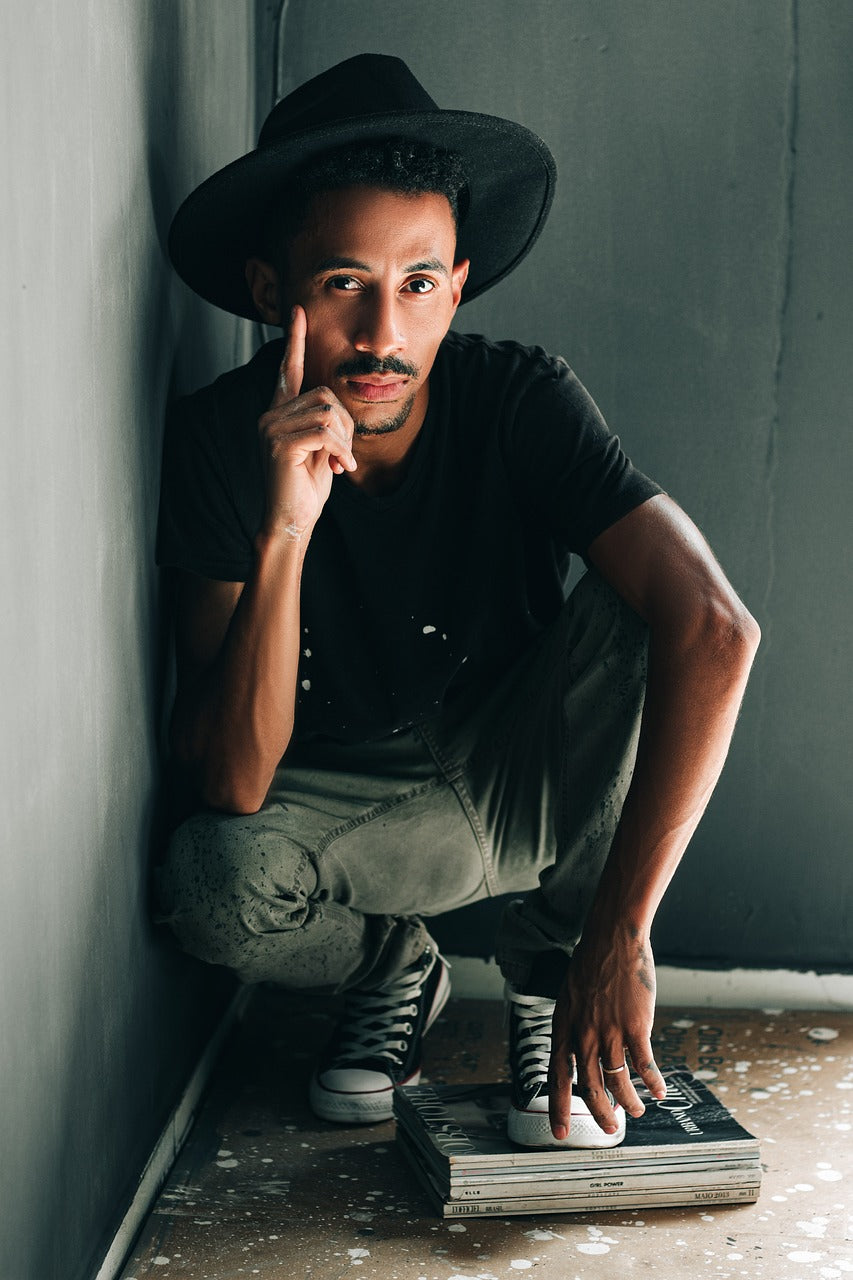 A man in a hat kneels against a wall in a room.