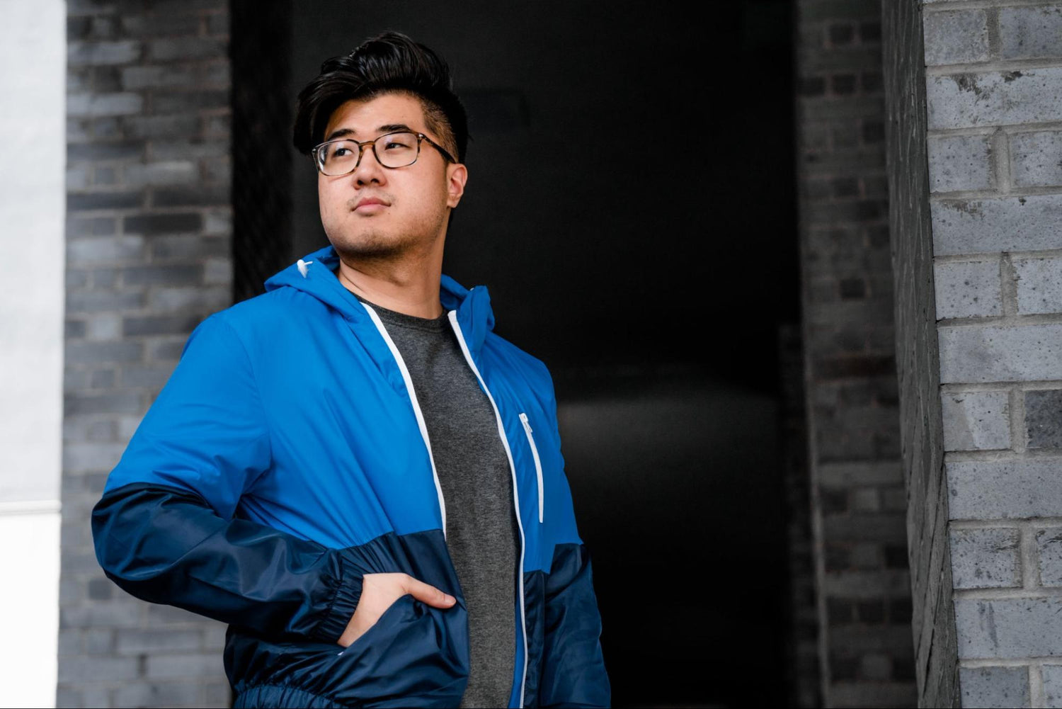 A man wearing glasses and a track jacket stands in a stone entranceway.