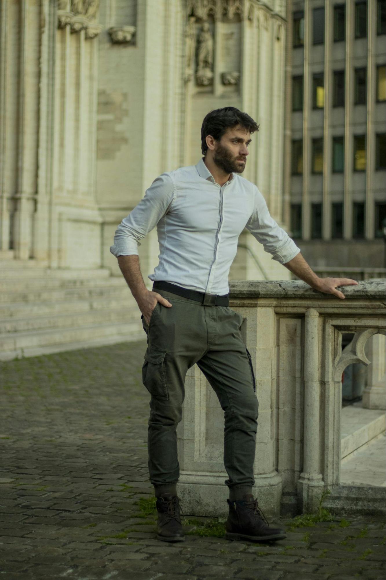 A man wearing green cargo pants and a white shirt stands outside a museum.